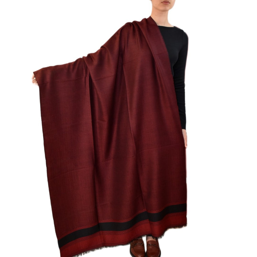 Person holding a large burgundy scarf with black trim on a white background